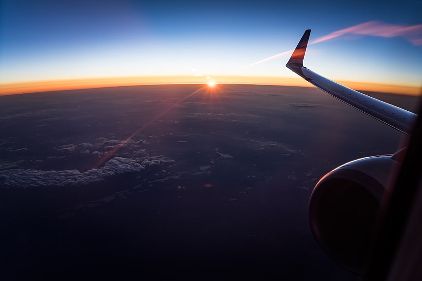 Airplane wing view of sunset over clouds and ocean