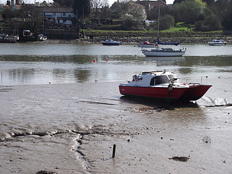 Red and white boat stranded on muddy riverbank at low tide