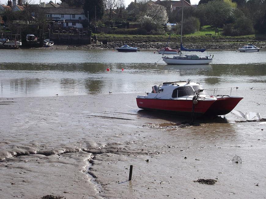 Red and white boat stranded on muddy riverbank at low tide