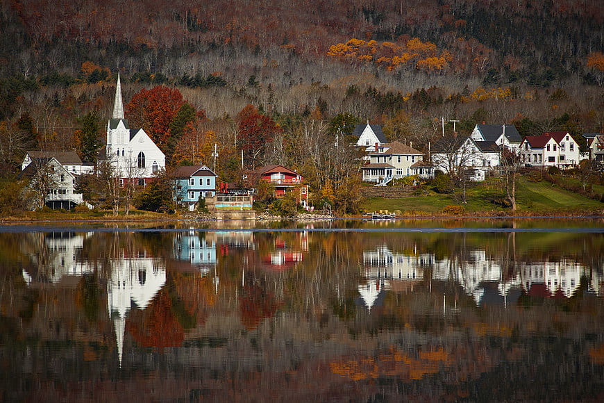 Autumn village with church and houses reflected in calm lake water