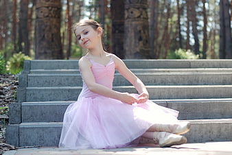 Young ballerina in pink tutu sitting on stone steps in a forest