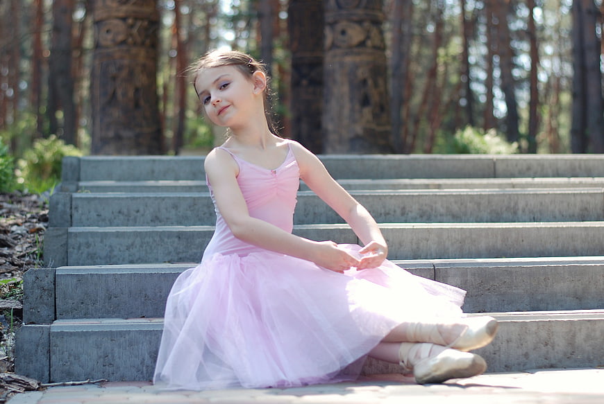 Young ballerina in pink tutu sitting on stone steps in a forest