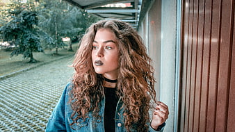 Portrait of young woman with curly hair and denim jacket outdoors