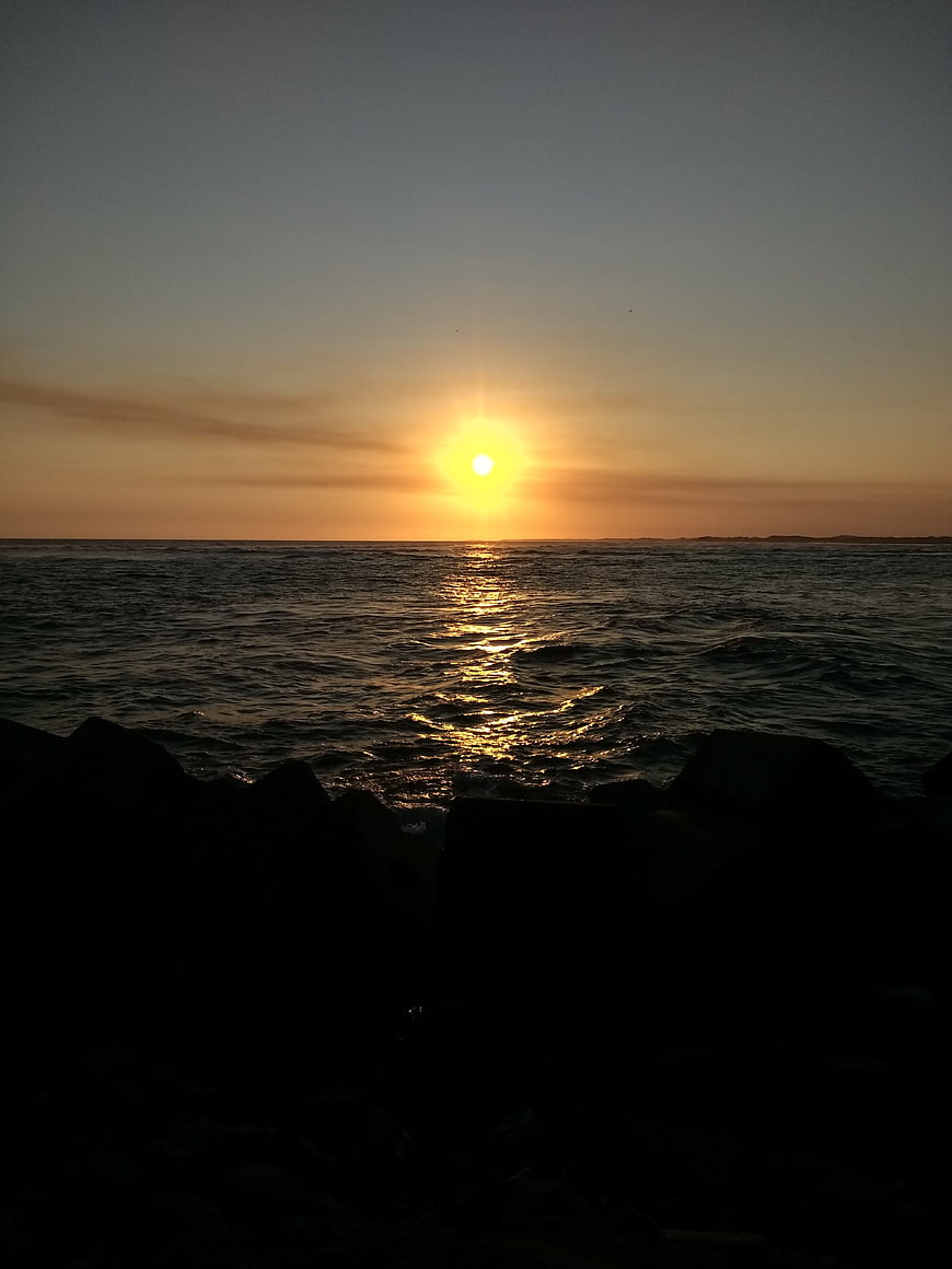 Sunset over ocean with silhouetted rocks in foreground