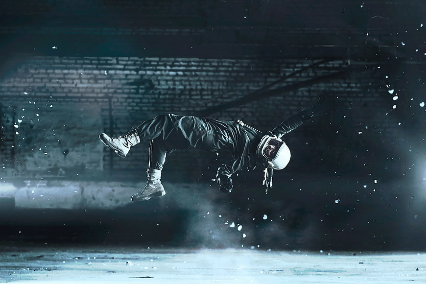 Motorcyclist in white helmet performing mid-air stunt in dark industrial setting