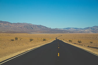Empty desert highway winding through arid landscape with mountains
