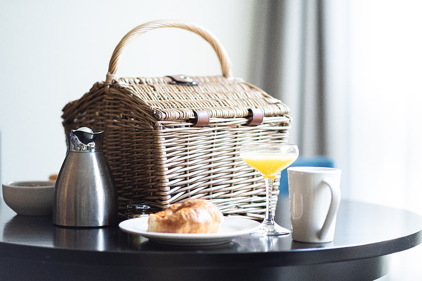 Wicker picnic basket with breakfast croissant and juice on table