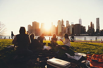 Friends Picnicking on Grass with City Skyline at Sunset
