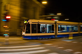 Blue and white tram moving through city street at night