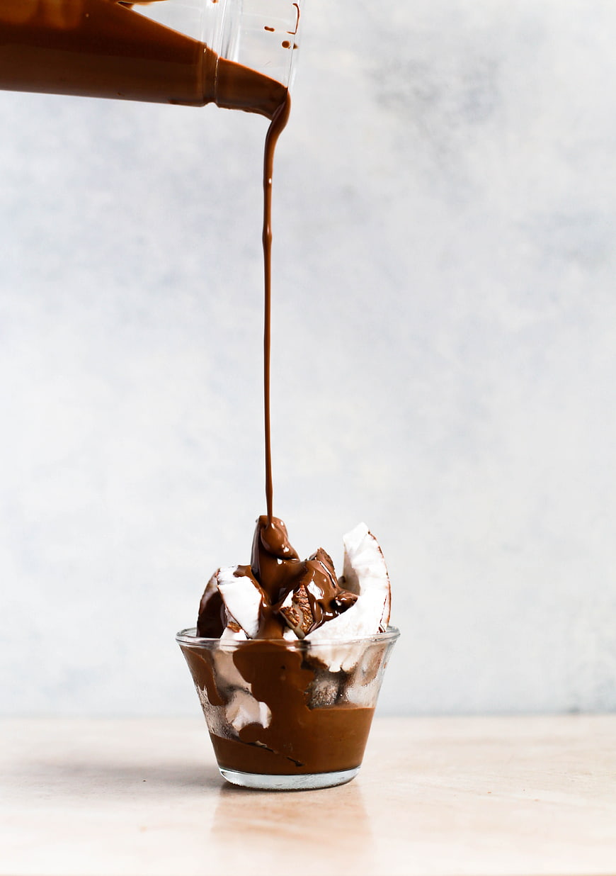 Pouring chocolate sauce on coconut dessert in glass cup