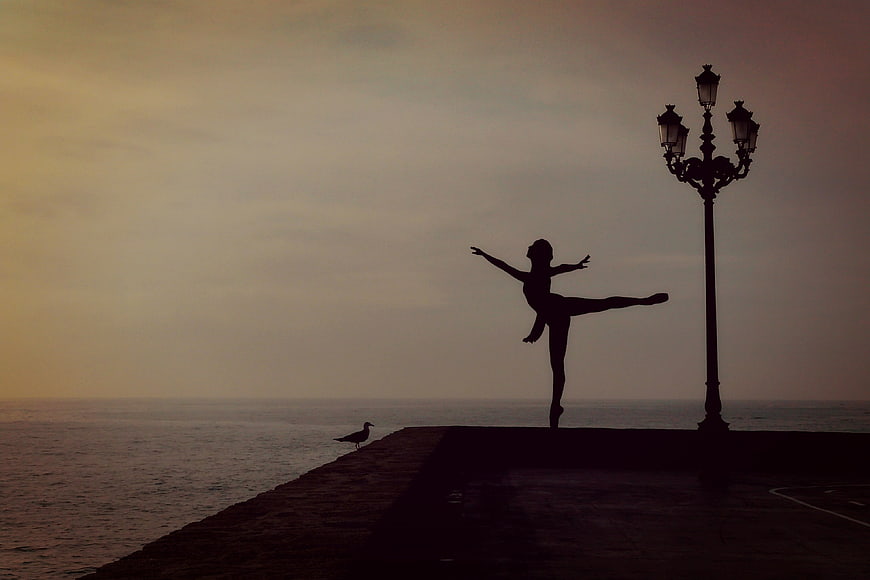 Silhouette of Ballet Dancer Performing by the Sea at Sunset