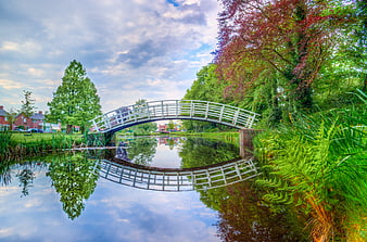 White arched bridge over calm pond with reflection