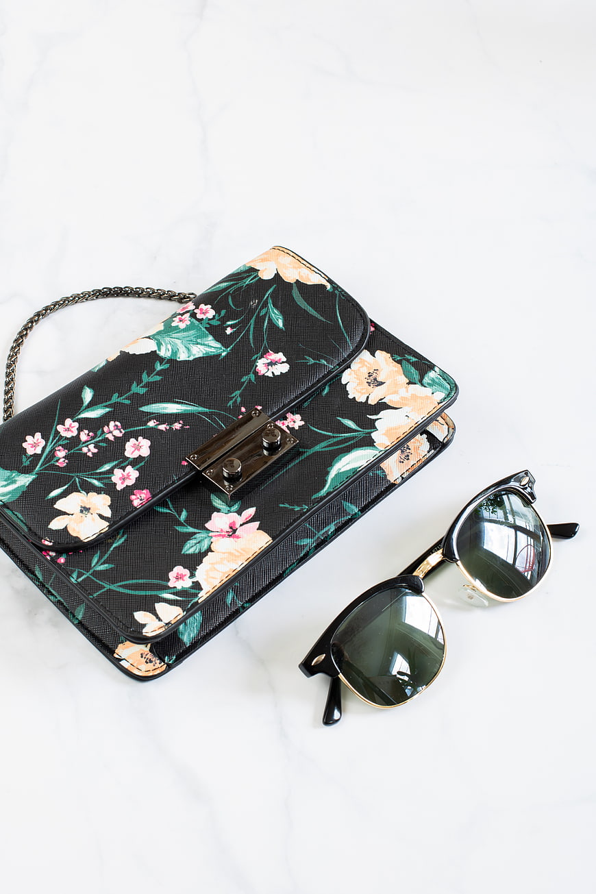 Floral black handbag and sunglasses on marble background