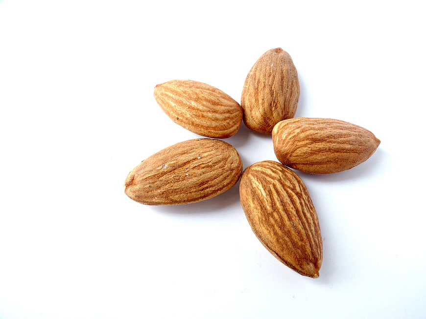 Five raw almonds arranged in a circle on white background