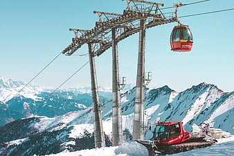 Red cable car and snow groomer on snowy mountain peak