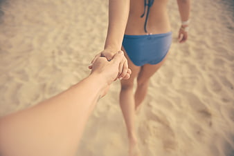 Romantic couple holding hands on a sandy beach in a blue bikini