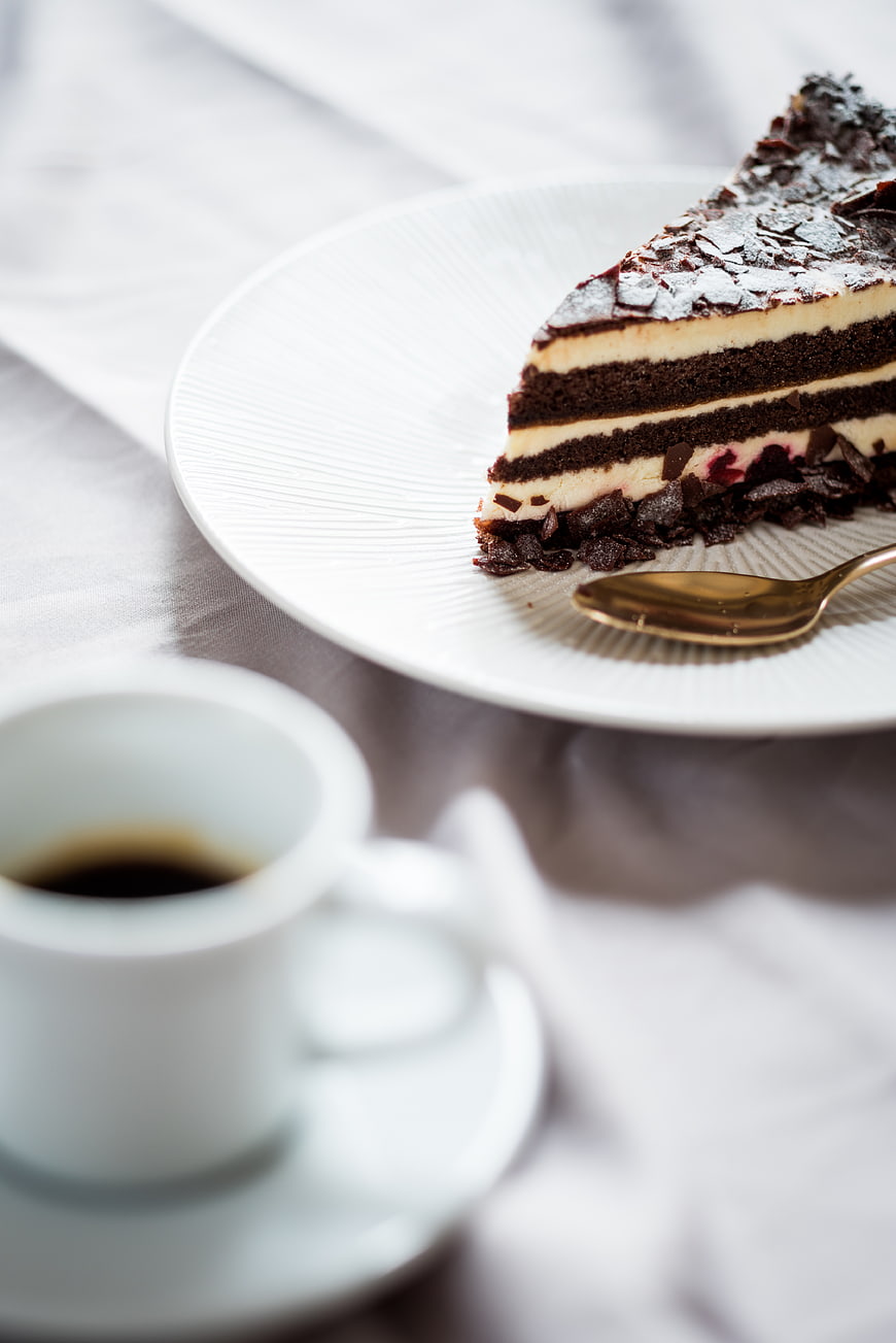 Slice of layered chocolate cake with coffee cup on white plate