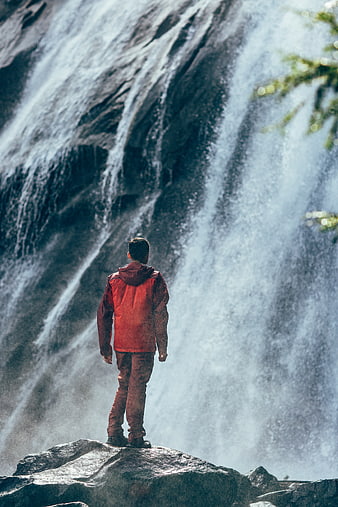 Man in Red Jacket Standing Before Massive Waterfall