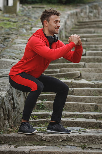 Athletic Man Squatting on Stone Steps in Red Hoodie