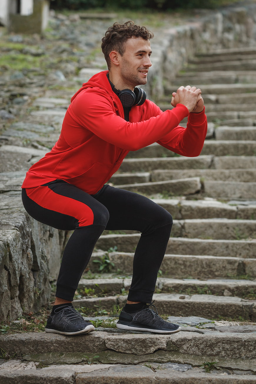Athletic Man Squatting on Stone Steps in Red Hoodie