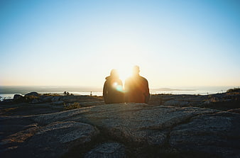 Couple Silhouette Sitting on Rocky Cliff at Sunset