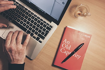 Overhead view of hands typing on laptop with red book and pen