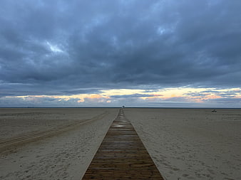 Wooden Boardwalk Leading to Ocean Horizon Under Dramatic Clouds