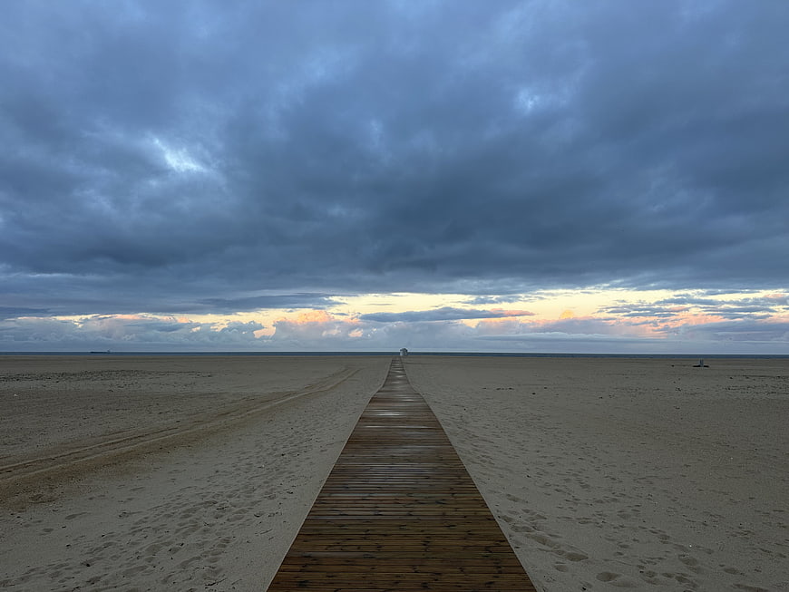 Wooden Boardwalk Leading to Ocean Horizon Under Dramatic Clouds