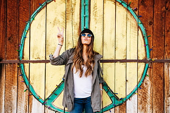 Woman making peace sign in front of wooden peace symbol mural