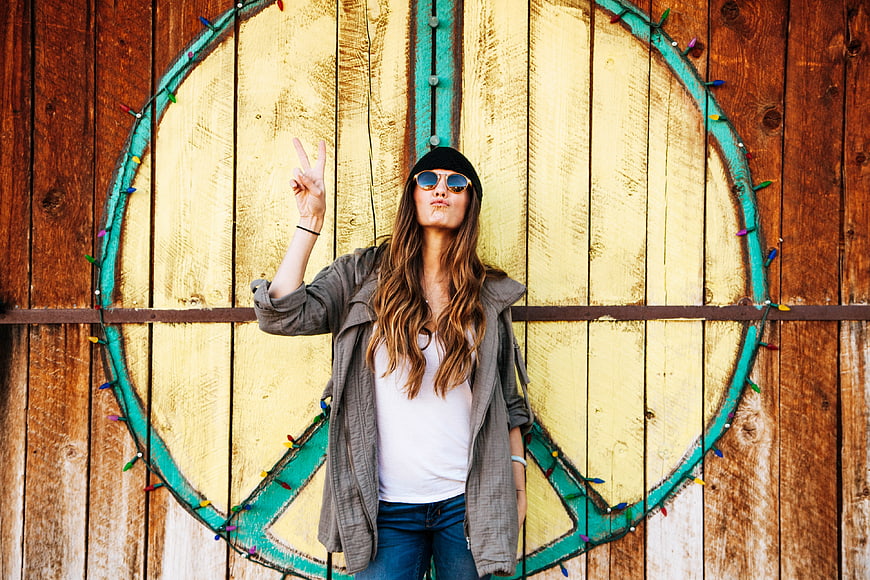 Woman making peace sign in front of wooden peace symbol mural