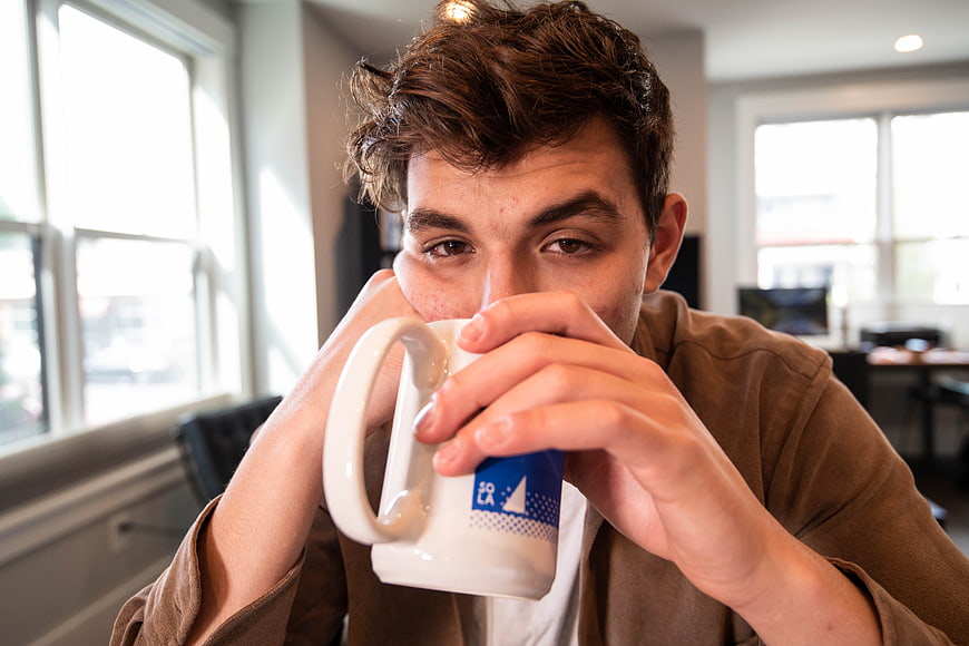 Young man drinking coffee from white mug in office