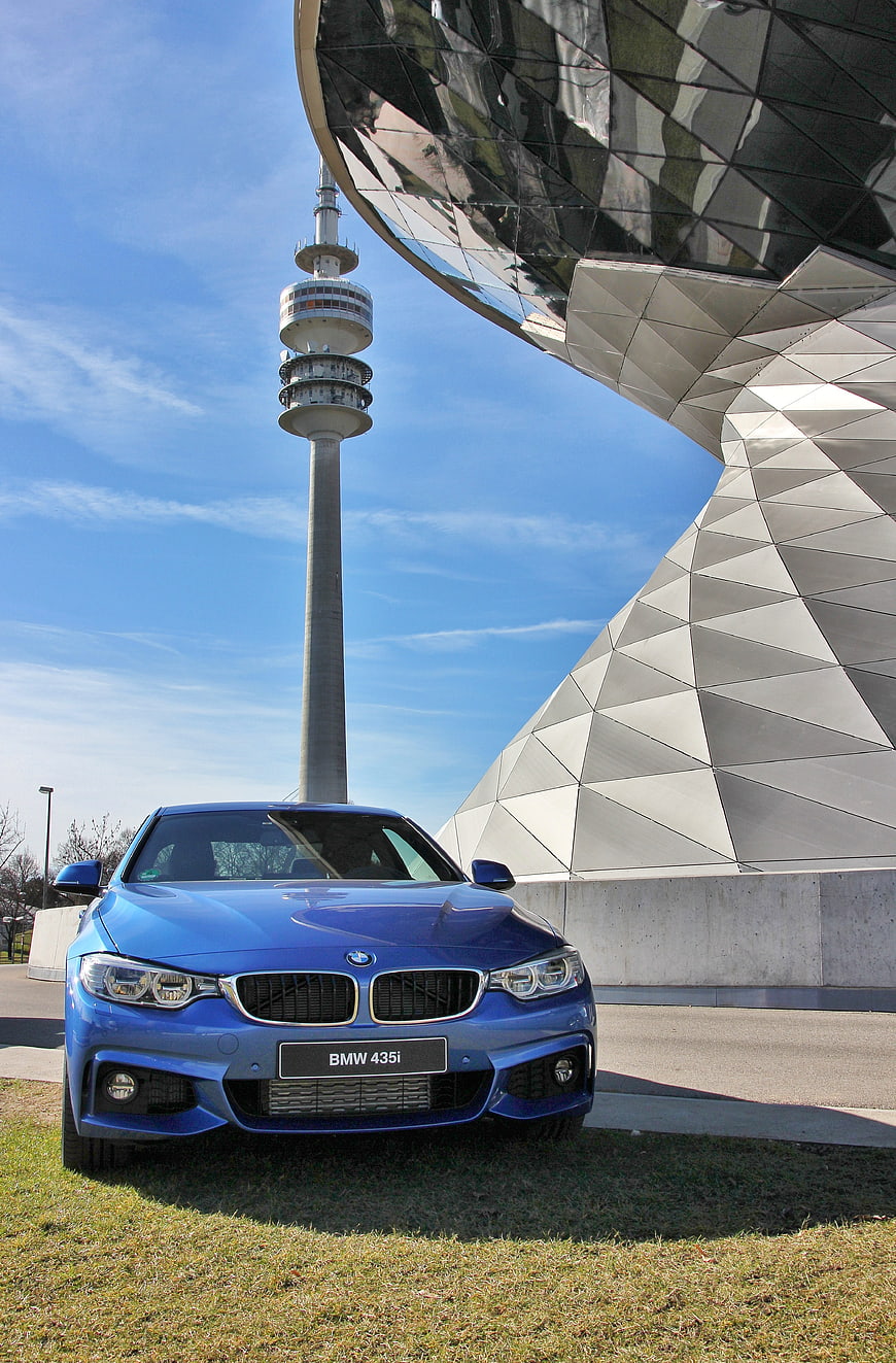 Blue BMW 435i parked in front of BMW World and Munich TV Tower