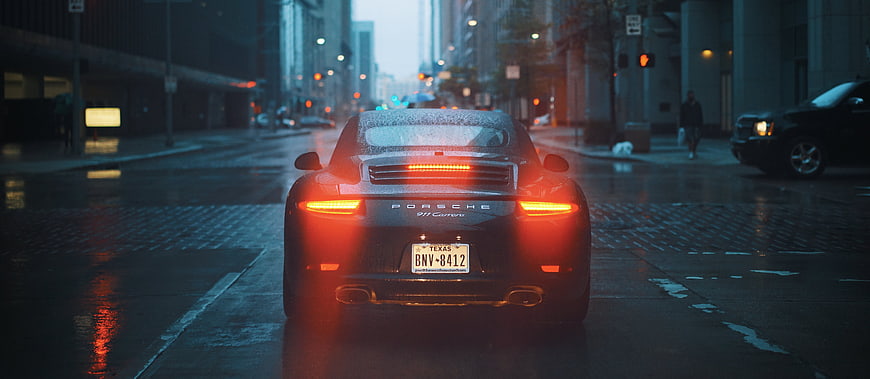 Rear view of Porsche 911 on wet city street at dusk