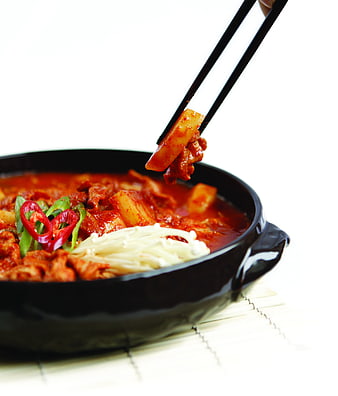 Korean spicy pork stew with kimchi and enoki mushrooms in black bowl