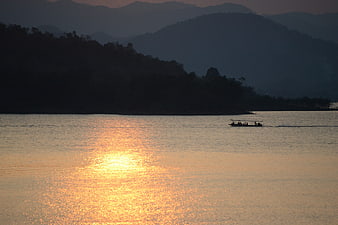 Longtail boat on lake at sunset with mountain silhouettes