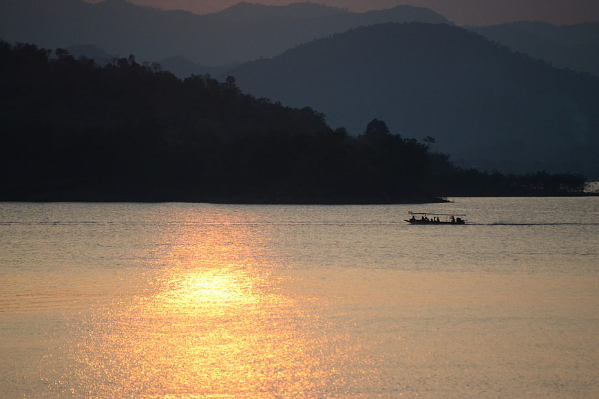 Longtail boat on lake at sunset with mountain silhouettes