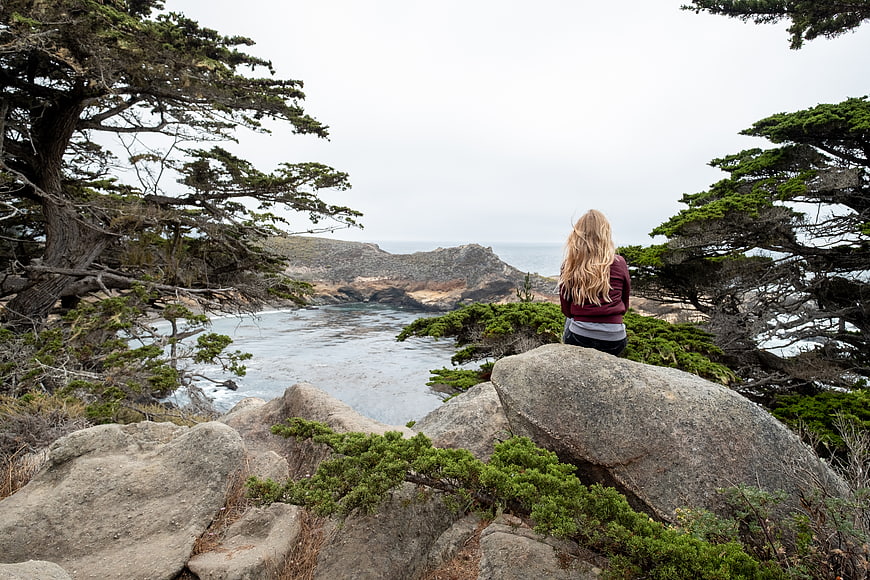 Woman sitting on rocky cliff overlooking ocean coastline