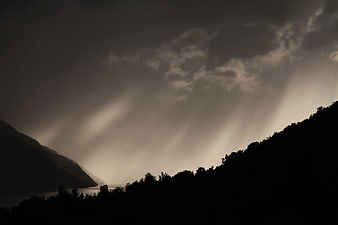 Dramatic sun rays breaking through clouds over mountain silhouette