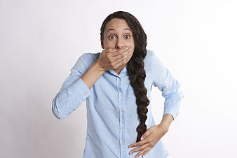 Surprised woman with long braid covering mouth in blue shirt