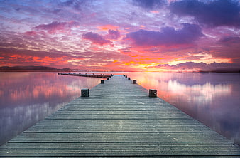 Wooden pier extending into calm lake at vibrant sunset