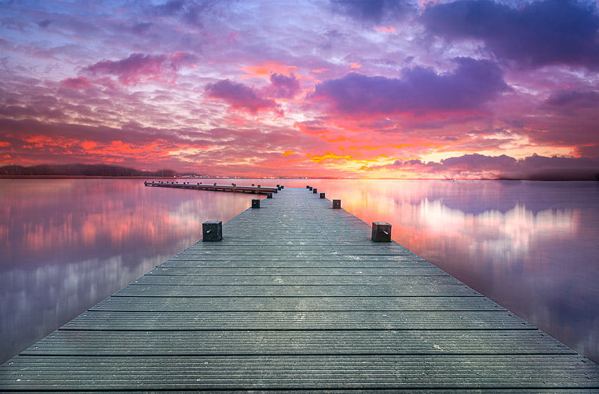 Wooden pier extending into calm lake at vibrant sunset