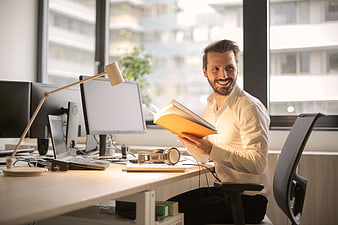 Smiling man reading book at modern office desk
