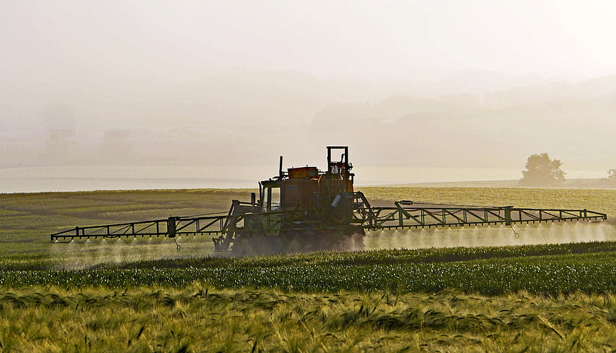 Agricultural sprayer machine treating crops in a misty field