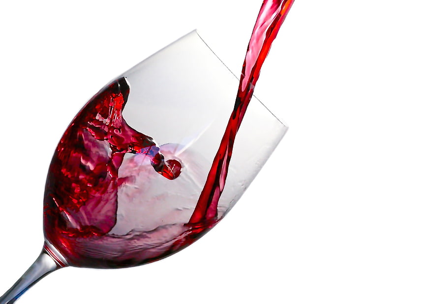 Red wine pouring into glass with dynamic splash on white background