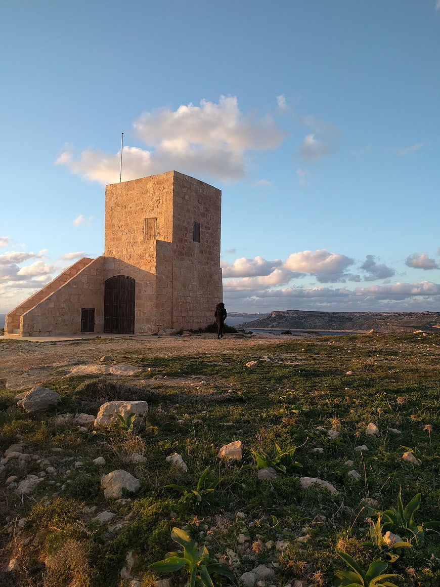 Solitary stone chapel on grassy hill at sunset