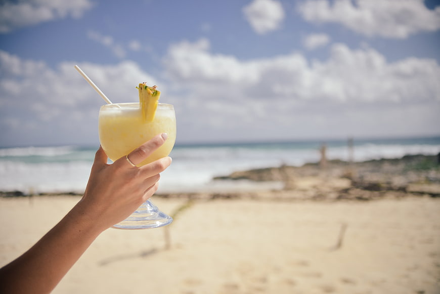 Hand holding pineapple cocktail on sunny beach