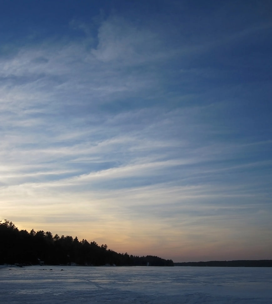 Frozen Lake Sunset with Silhouetted Forest and Cloudy Sky