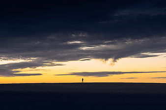 Silhouette of a person standing alone on a vast horizon at sunset