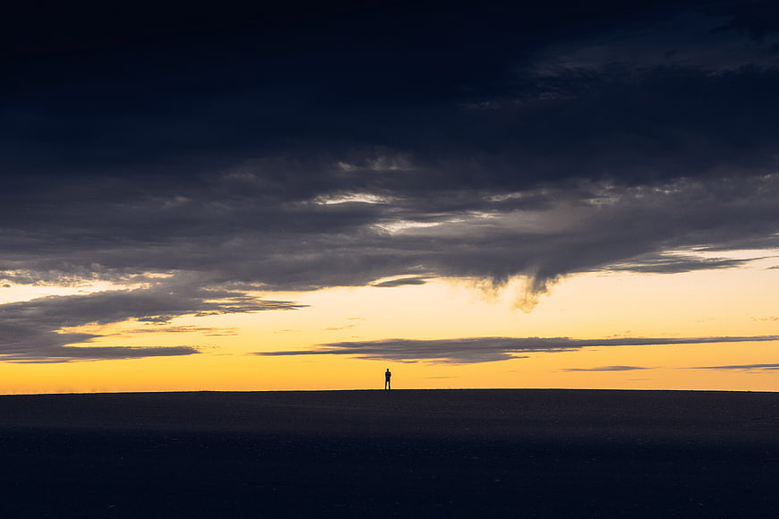 Silhouette of a person standing alone on a vast horizon at sunset
