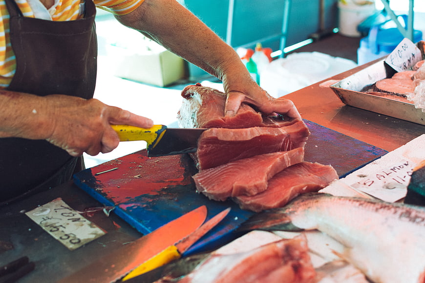 Fishmonger slicing fresh tuna steaks at market